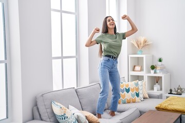 Young beautiful hispanic woman smiling confident dancing on sofa at home