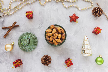 Candied or sugared almonds with honey and cinnamon in bowl on gray with Christmas decoration background. Traditional Christmas sweets for holidays. Top view, copy space