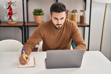 Young hispanic man using laptop sitting on table at home