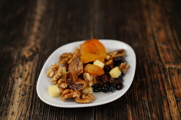 Dried fruits mixed on a white plate on wooden background. Apricot, fig, walnut, raisin, and kasha cheese appetizer (meze). 