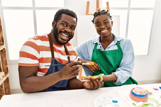 African american painter couple smiling happy painting hands sitting on the table at art studio.