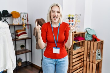 Young caucasian woman working as manager at retail boutique shouting with crazy expression doing rock symbol with hands up. music star. heavy concept.