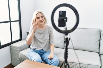 Young caucasian woman recording vlog tutorial with smartphone at home showing and pointing up with fingers number four while smiling confident and happy.