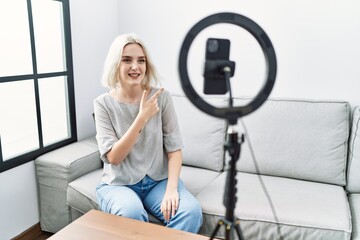 Fototapeta na wymiar Young caucasian woman recording vlog tutorial with smartphone at home cheerful with a smile of face pointing with hand and finger up to the side with happy and natural expression on face