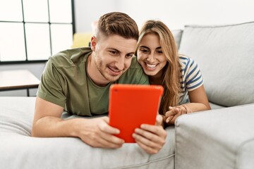 Young hispanic couple using touchpad lying on the sofa at home.