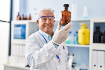 Senior man wearing scientist uniform holding bottle at laboratory
