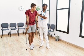 Two men physiptherapist and patient having medical consultation walking using crutches at hospital...