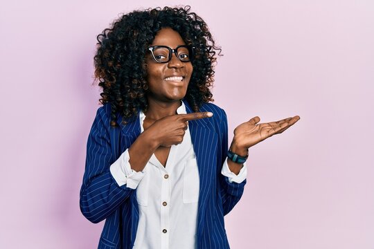 Young african american woman wearing business clothes and glasses amazed and smiling to the camera while presenting with hand and pointing with finger.