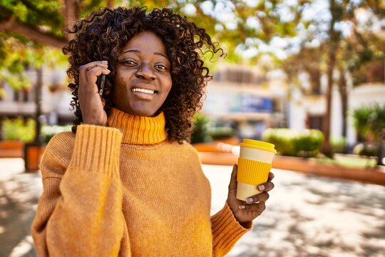African american woman talking on the smartphone drinking coffee at park