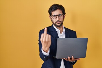 Handsome latin man working using computer laptop showing middle finger, impolite and rude fuck off expression