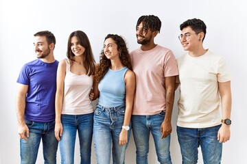 Obraz premium Group of young people standing together over isolated background looking away to side with smile on face, natural expression. laughing confident.