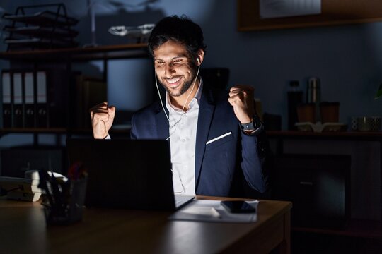 Handsome latin man working at the office at night screaming proud, celebrating victory and success very excited with raised arms