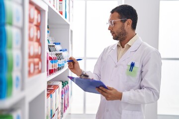 Young man pharmacist writing on document organize shelving at pharmacy