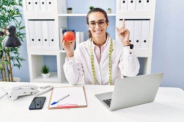 Young hispanic woman working dietitian clinic surprised with an idea or question pointing finger...