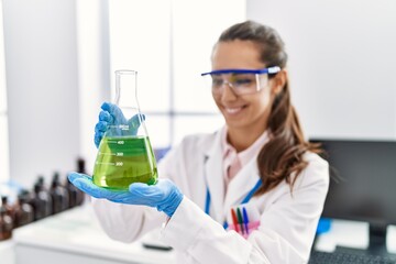 Young hispanic woman wearing scientist uniform holding test tube at laboratory