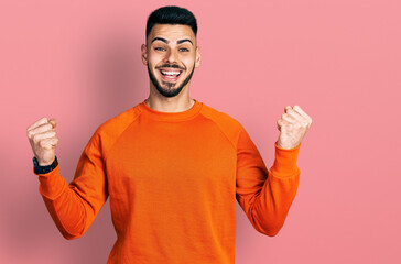 Young hispanic man with beard wearing casual orange sweater celebrating surprised and amazed for success with arms raised and open eyes. winner concept.