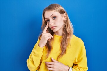 Fototapeta premium Young caucasian woman standing over blue background pointing to the eye watching you gesture, suspicious expression