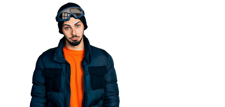 Young hispanic man with beard wearing snow wear and sky glasses depressed and worry for distress, crying angry and afraid. sad expression.