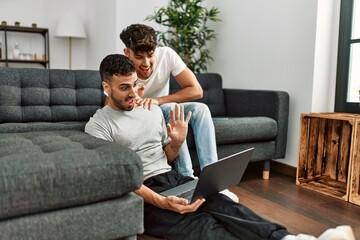 Two hispanic men couple hugging each other having video call at home