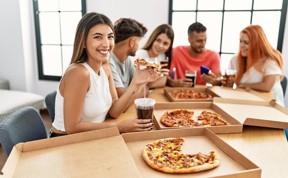 Group of young people smiling happy eating italian pizza sitting on the table at home