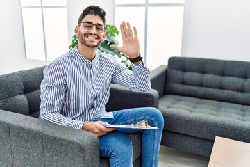 Young psychologist man at consultation office waiving saying hello happy and smiling, friendly welcome gesture © Krakenimages.com