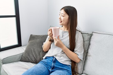 Young asian woman drinking cup of coffee sitting on the sofa at the living room