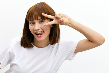 a funny, playful, emotional woman makes a funny face, showing her tongue and holding two fingers near her eye as a sign of victory. Horizontal photo with an empty space for inserting an advertising