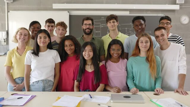 Big group portrait of multiracial high school student friends standing with teacher at classroom. Millennial classmate people smiling at camera together in college. High quality 4k footage