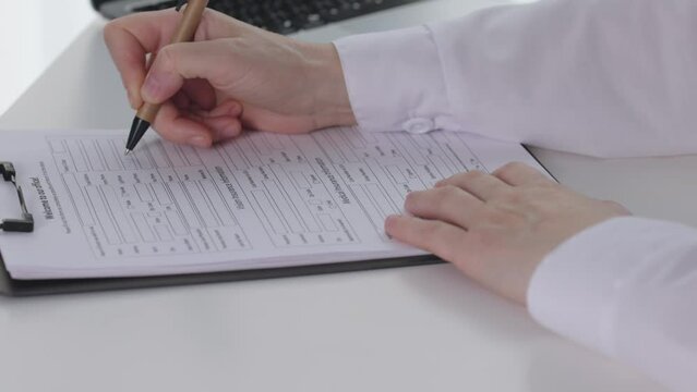 close-up doctor hands filling in writing medical form papers on desk office room. female hands in white doing paperwork at table write pen in papers docs black clipboard. concept healthcare medicine