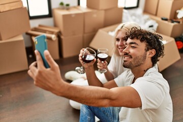 Young beautiful couple toasting with red wine and making selfie at new home