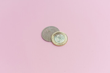 Moneda mexicana nueva de 10 pesos y moneda mexicana antigua de 5 pesos sobre fondo rosa.