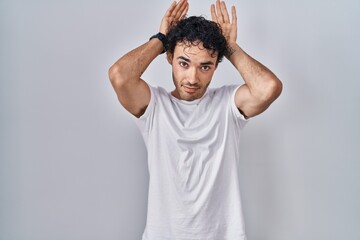 Hispanic man standing over isolated background doing bunny ears gesture with hands palms looking cynical and skeptical. easter rabbit concept.