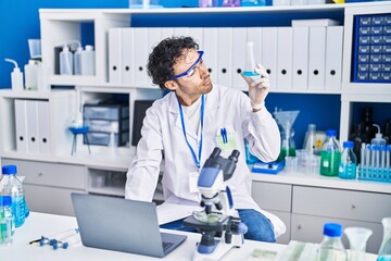 Young hispanic man scientist using laptop holding test tube at laboratory