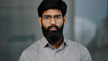 Portrait of serious handsome arabic hispanic young male bearded guy in eyeglasses wear shirt stands...