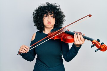 Young middle east woman playing violin puffing cheeks with funny face. mouth inflated with air,...