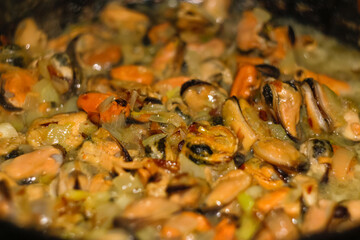 Defocus mussels dish on pan. Delicious seafood mussels with parrot and onion. Heap of peeled mussels with spoon close-up on a dark background. Seafood. Delicious sauce. Out of focus