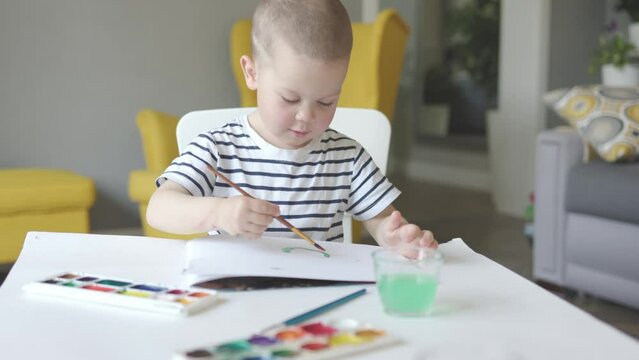 child elementary age sitting home painting drawing art class using water paint. early home education concept. kid boy draws aquarelle creative occupation, children kids artistic development. school 