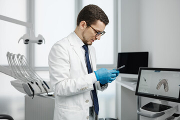 Handsome male dentist using smartphone in dental office