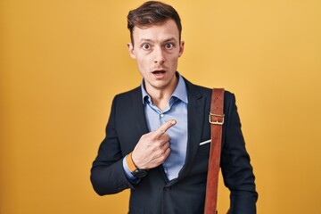 Caucasian business man over yellow background surprised pointing with finger to the side, open mouth amazed expression.