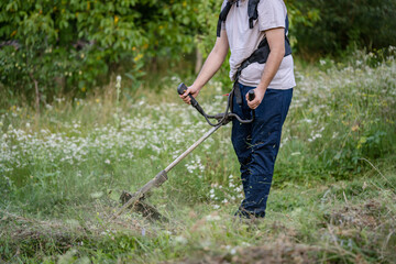 caucasian man farmer using string trimmer to cut grass brush cutter