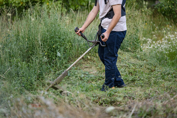 caucasian man farmer using string trimmer to cut grass brush cutter