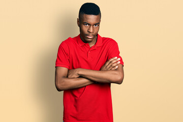 Young african american man wearing casual red t shirt skeptic and nervous, disapproving expression on face with crossed arms. negative person.