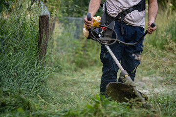 Obraz premium caucasian man farmer using string trimmer to cut grass brush cutter