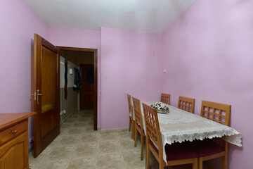 Wooden dining table with white tablecloth and matching chairs in a room with fuchsia painted walls