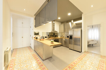 Large open kitchen with industrial style stainless steel cabinets and appliances, wood countertops with island and gray colored floor and hydraulic tile