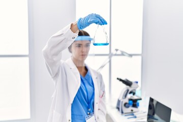 Fototapeta na wymiar Young hispanic woman wearing scientist uniform holding test tube at laboratory