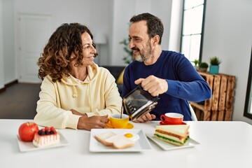 Middle age hispanic couple smiling happy sitting on the table having breakfast at home.