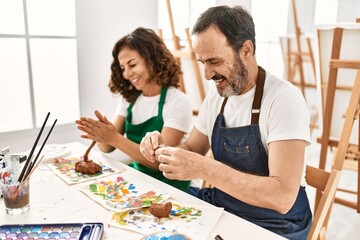 Two middle age students smiling happy modeling clay sitting on the table at art school.