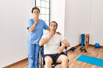 Fototapeta premium Hispanic middle age man sitting on wheelchair and nurse at rehabilitation clinic covering mouth with hand, shocked and afraid for mistake. surprised expression