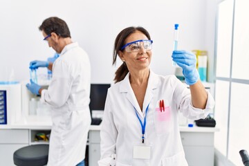 Middle age man and woman partners wearing scientist uniform holding test tube at laboratory